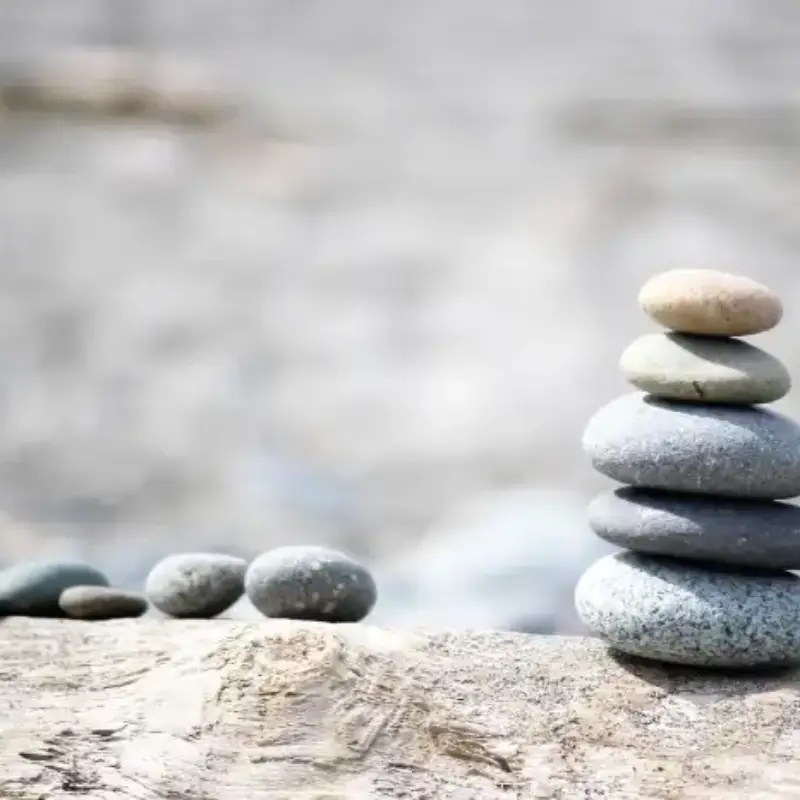 home_bottom_stones Steintürmchen aus Kieselsteinen auf einem quer liegenden alten Baumstamm.